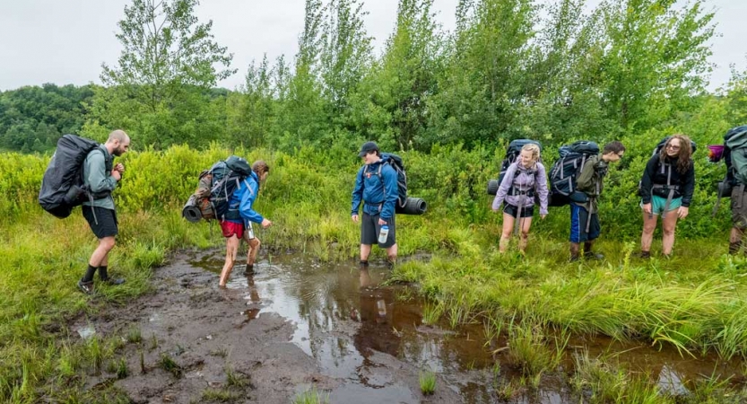 A group of backpackers navigate across a muddy field. 